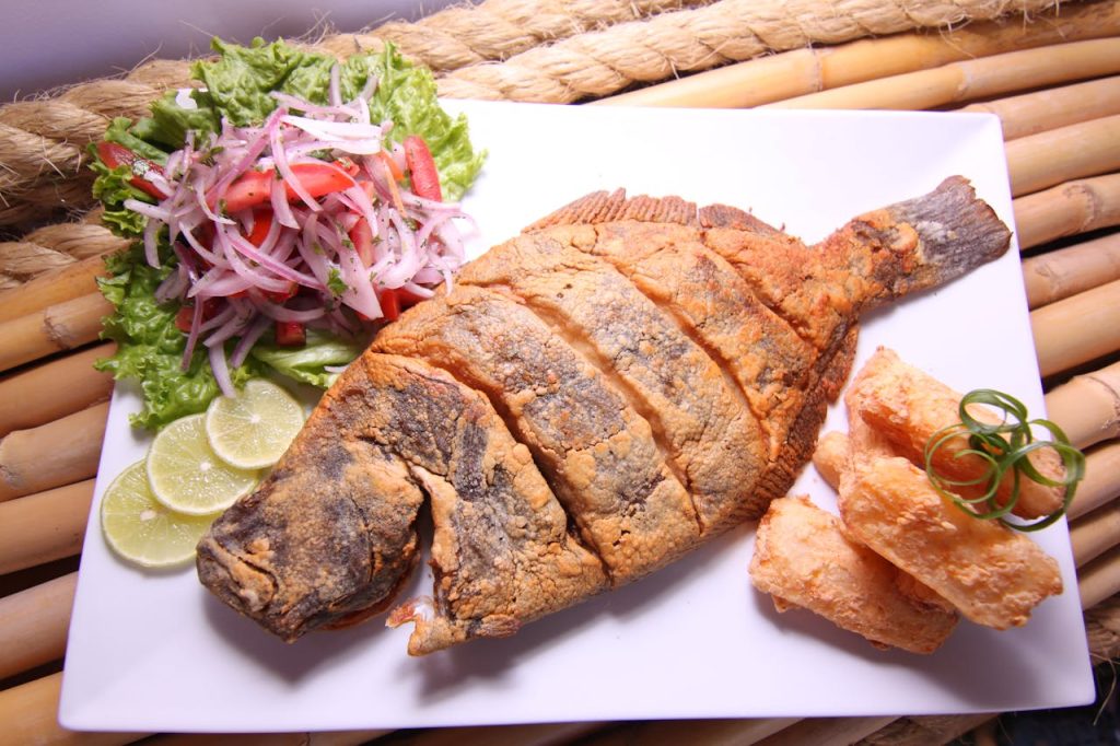 Deliciously prepared Peruvian fried fish plated with fresh salad, lime slices, and crispy yuca.